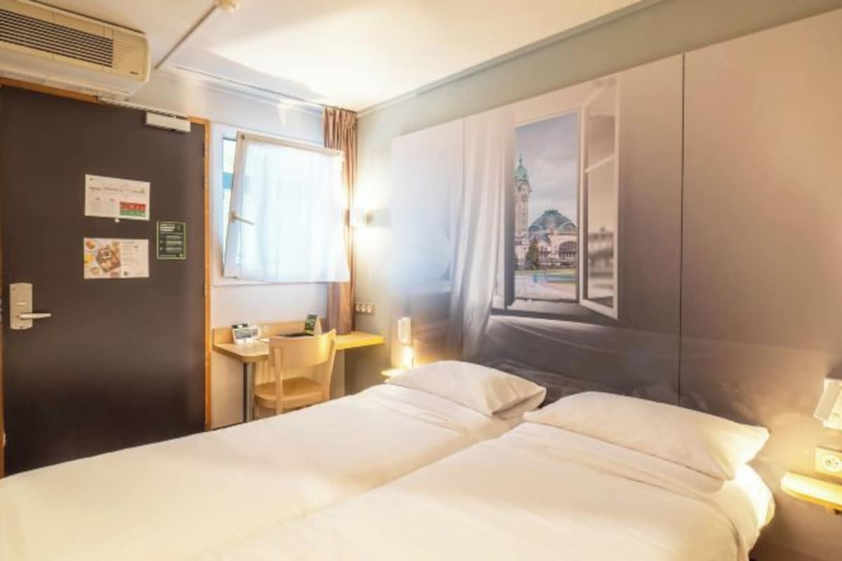A hotel room with a bed, a desk, a chair, and a wall with a window view.