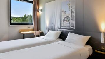 Une chambre d’hôtel avec deux lits, un bureau et une fenêtre donnant sur un espace verdoyant et un immeuble.