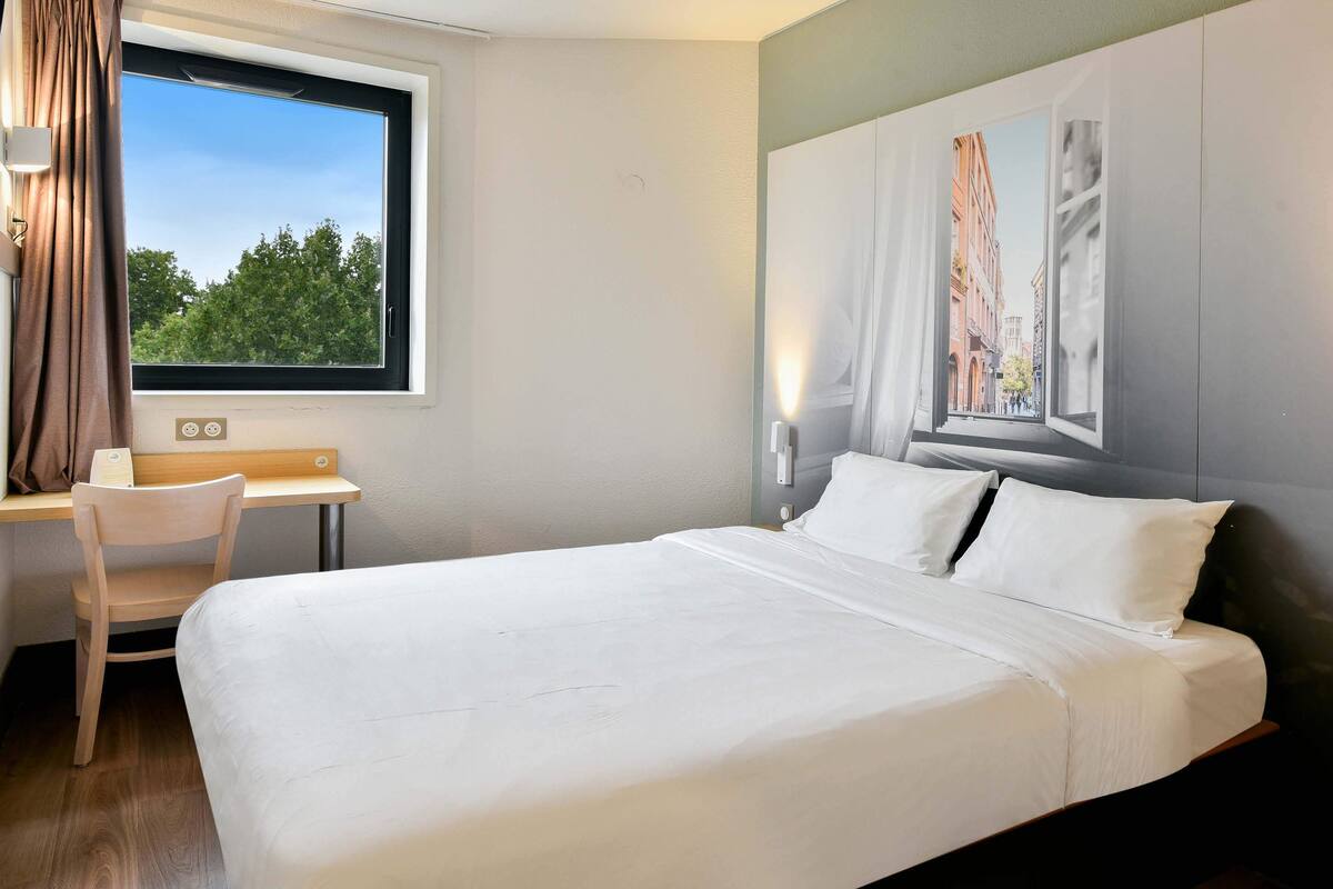 A hotel room with a large bed, a desk, and a window with curtains.