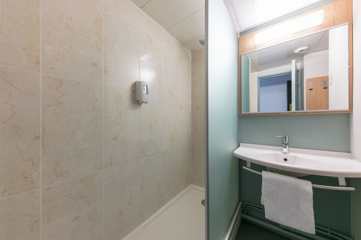 Un baño con ducha, lavamanos y espejo.