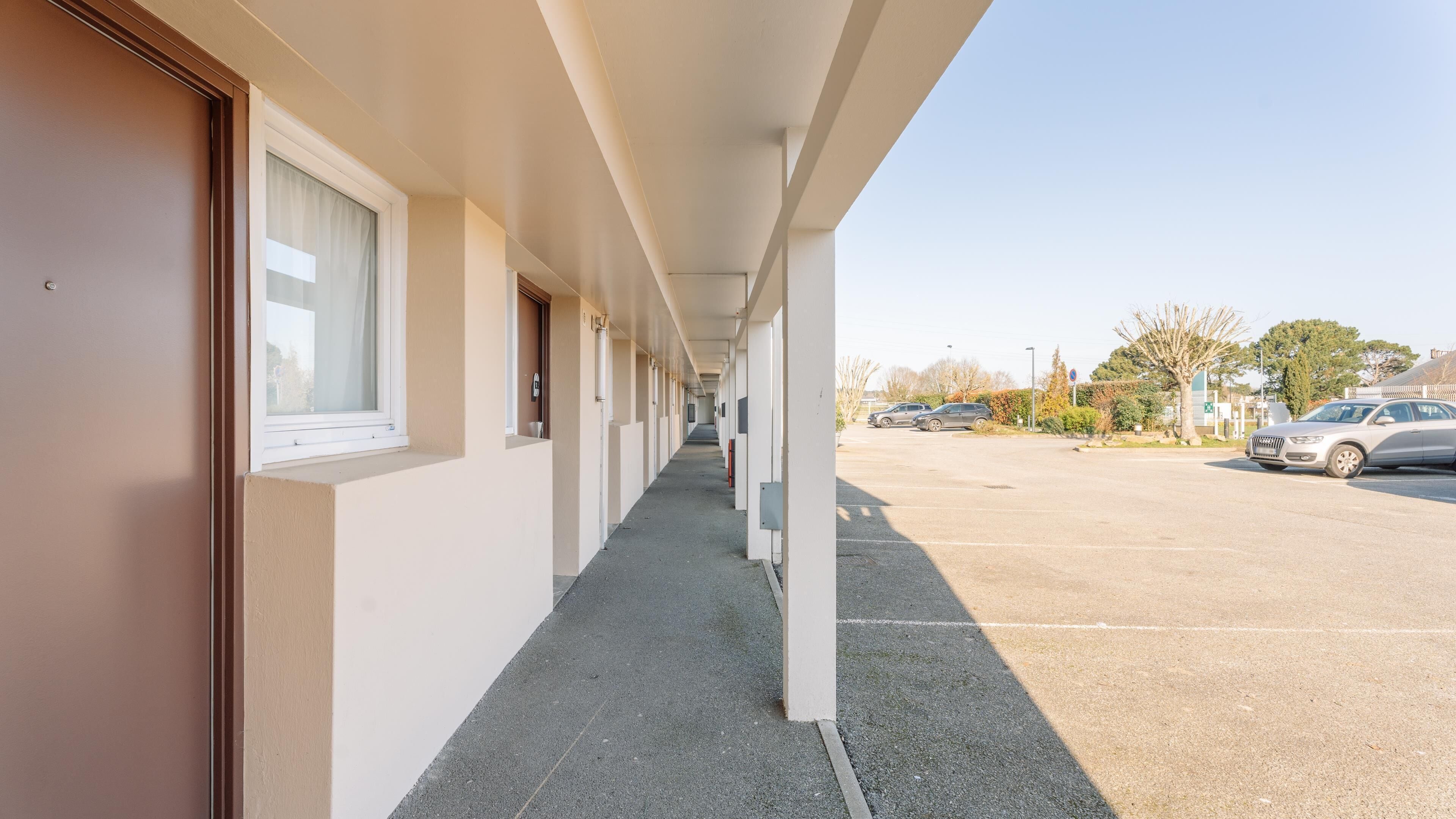 A corridor with doors, windows, and a parking lot with cars.
