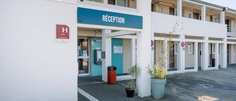 A hotel reception with a blue sign, a wheelchair-accessible entrance, and a security camera.