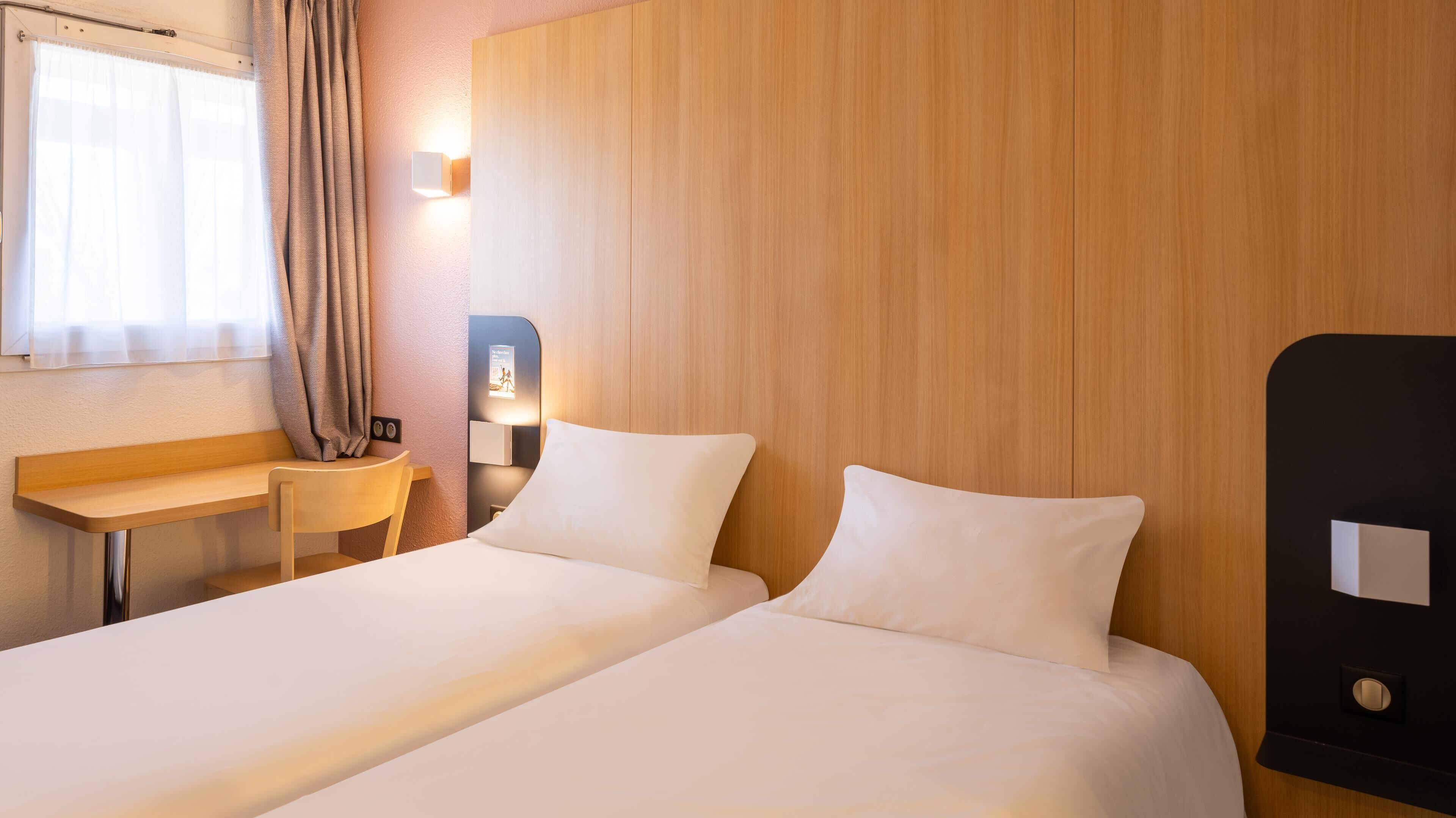 Habitación de hotel con dos camas, un escritorio, una silla y un cabecero de madera.