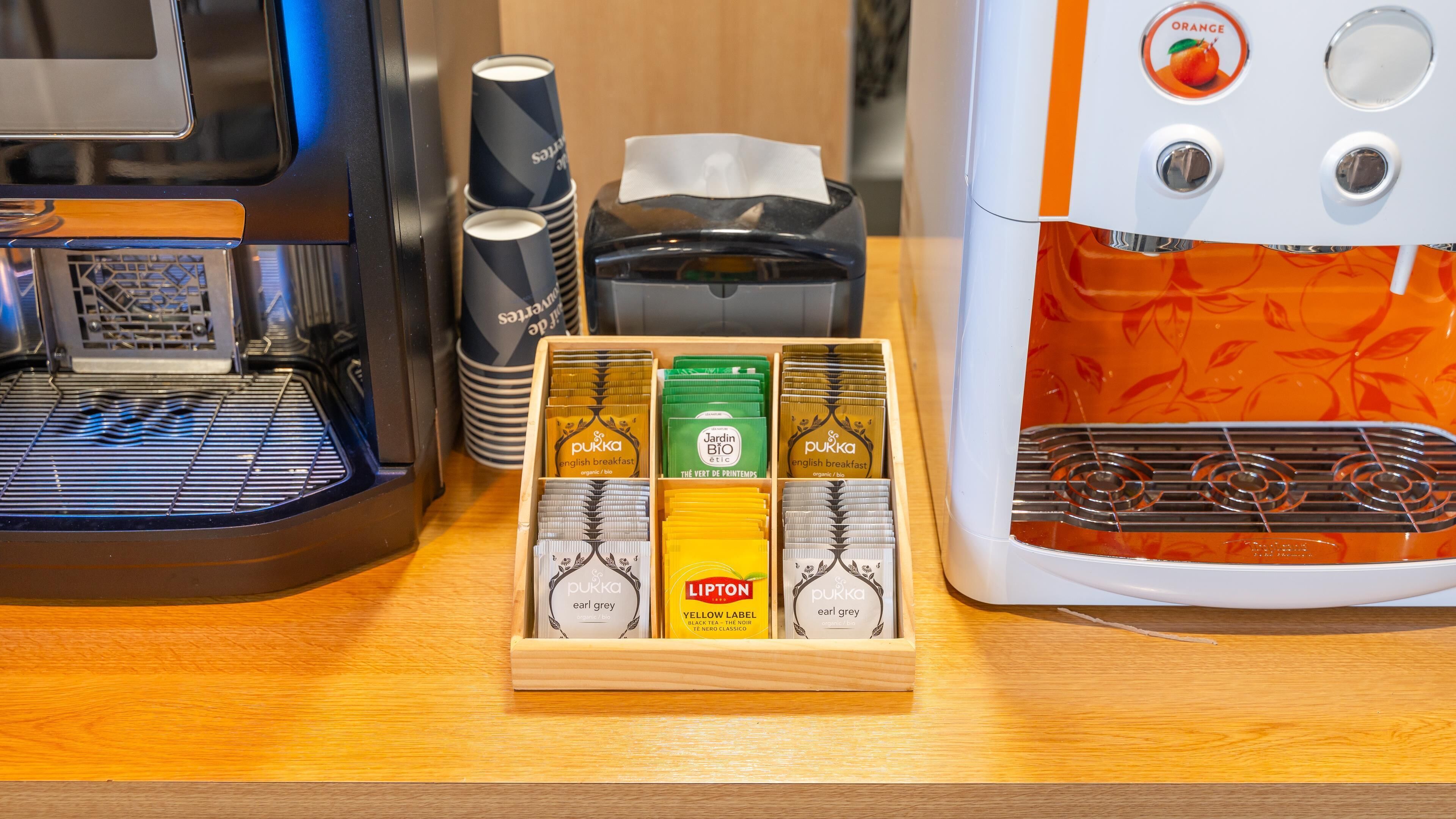 Una cafetera, una pila de vasos desechables y una presentación de cápsulas de café.