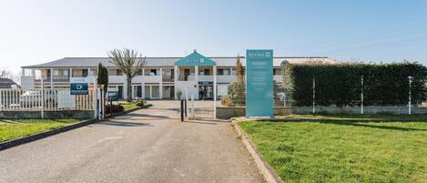 A building with a sign reading 'Kyriad ECO' and a welcome sign with amenities listed.