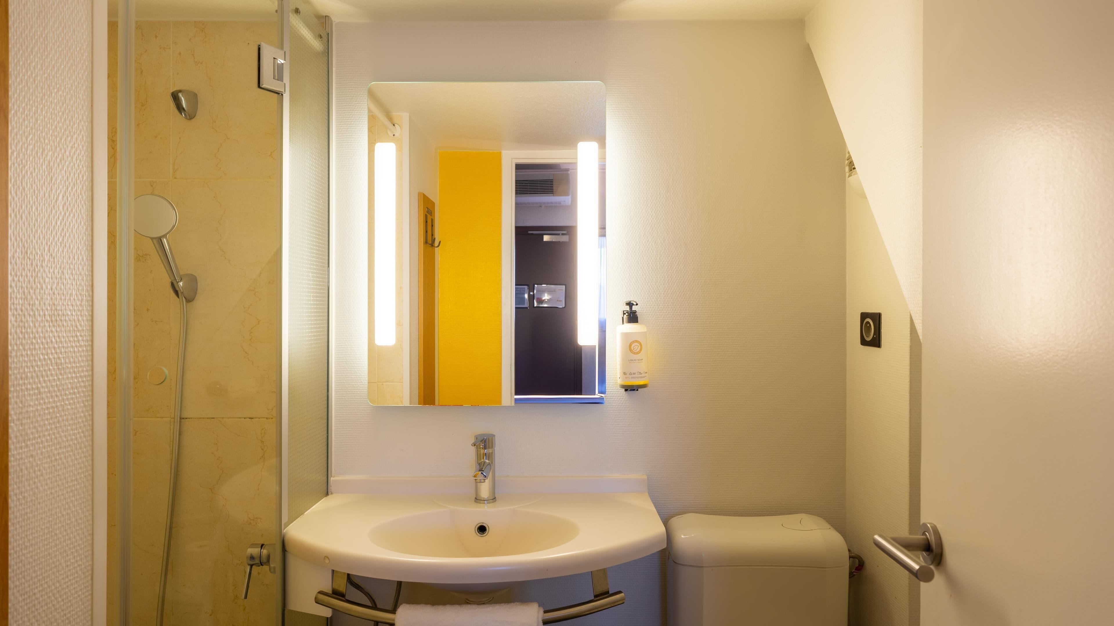A bathroom with a shower, sink, toilet, and a mirror.