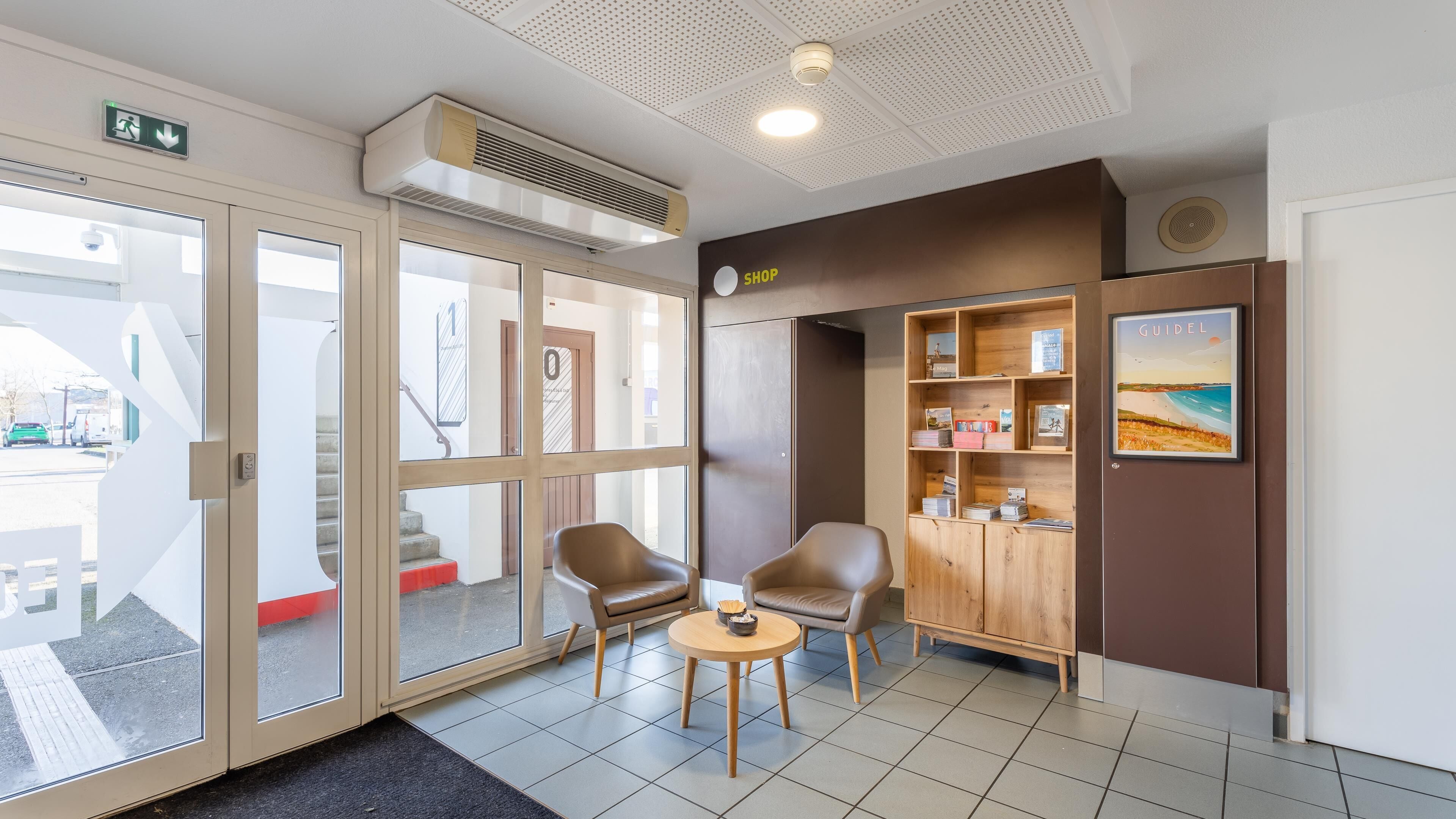 Een hotelhal met een receptiebalie, een boekenplank vol boeken, een ingelijst schilderij aan de muur en een trap naar de bovenverdieping.