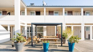 A modern building with a covered outdoor seating area, potted plants, and a clear sky. - Kyriad ECO - Lorient Lanester (Lanester)