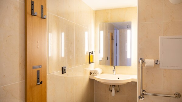 A modern bathroom with a sink, mirror, towel, and hand sanitizer.