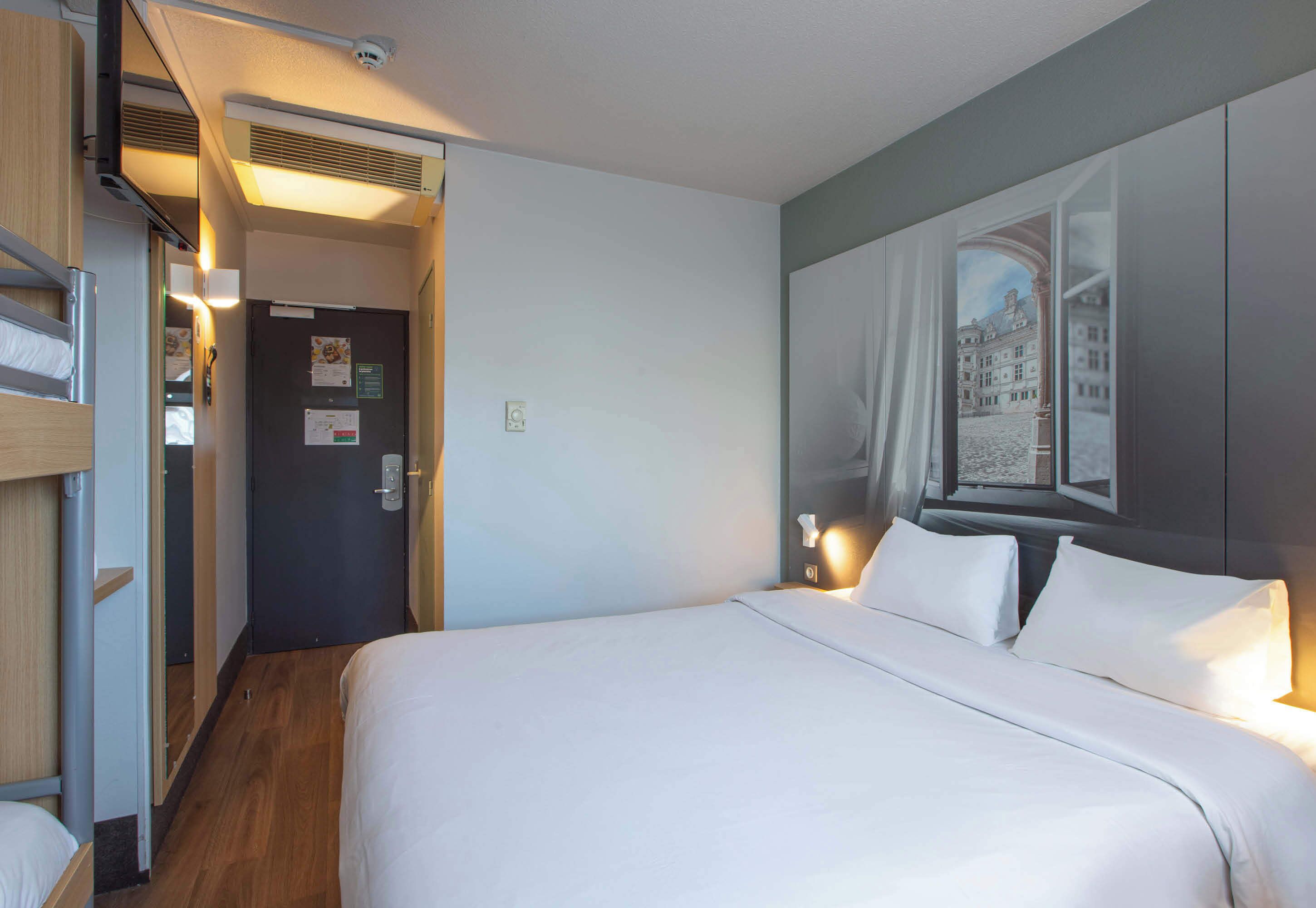 A hotel room with a bed, a door, and a wall with a framed picture.