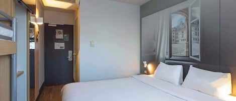 A hotel room with a bed, a door, and a wall with a framed picture.