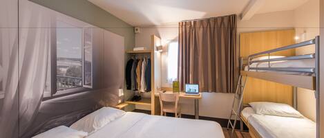 Quarto de hotel com uma cama grande, uma escrivaninha com um laptop, um guarda-roupa e vista para o exterior.