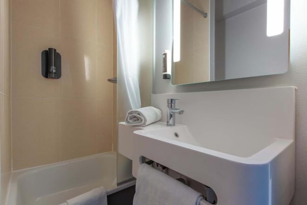 A modern bathroom with a white sink, a mirror, and a shower area.