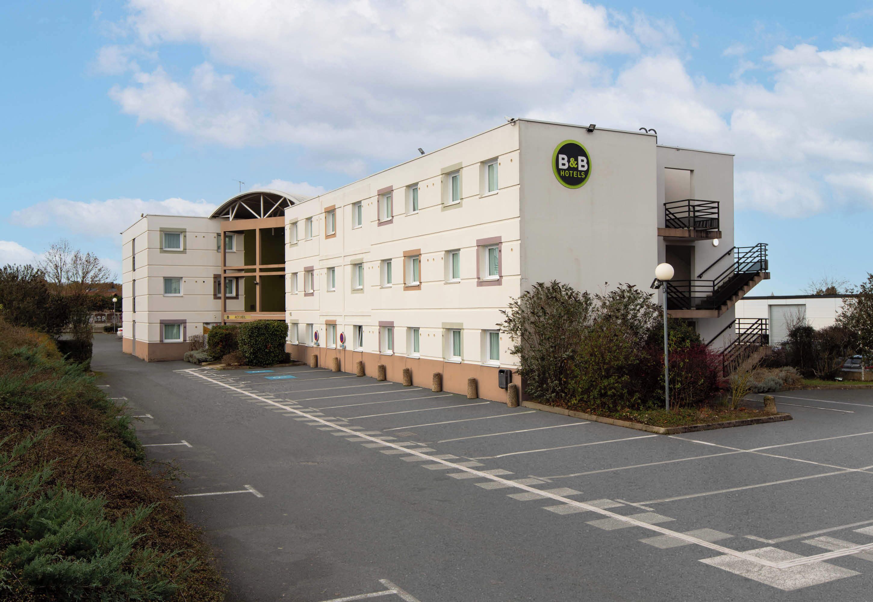 A B&B hotel with a modern design, featuring a parking lot and a small garden area.