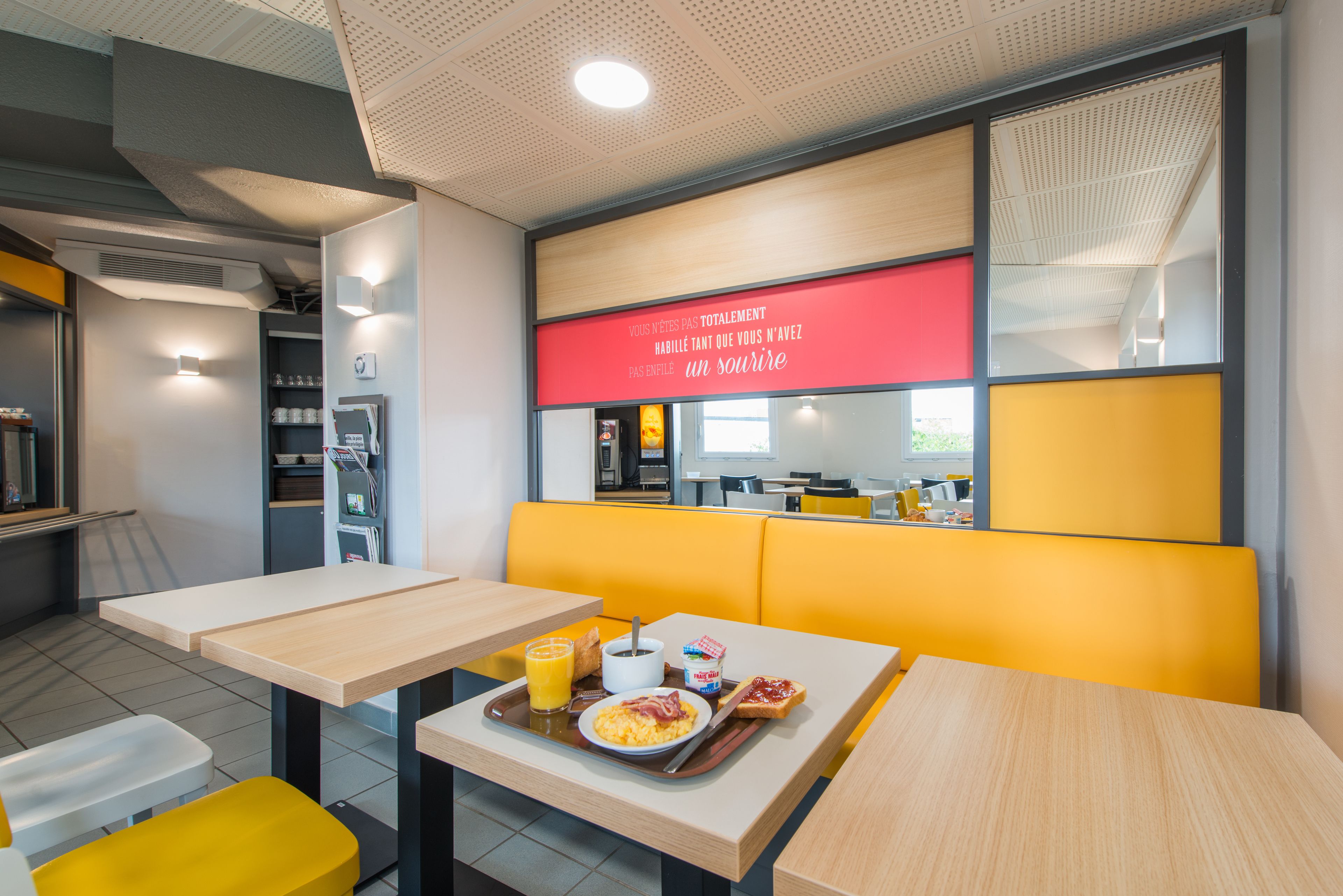 A modern dining area with yellow booths and wooden tables, featuring breakfast items like eggs, toast, and orange juice.