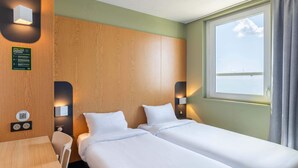 Habitación de hotel con dos camas, cabecero de madera, una mesita y ventana con vista al mar.
