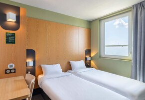 Habitación de hotel con dos camas, cabecero de madera, una mesita y ventana con vista al mar.