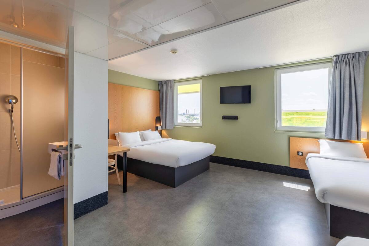 A hotel room with a bed, a desk, a TV, a shower, and a window with a view.