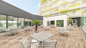 Un patio al aire libre con mesas y sillas, una palmera y vista a un edificio de hotel.