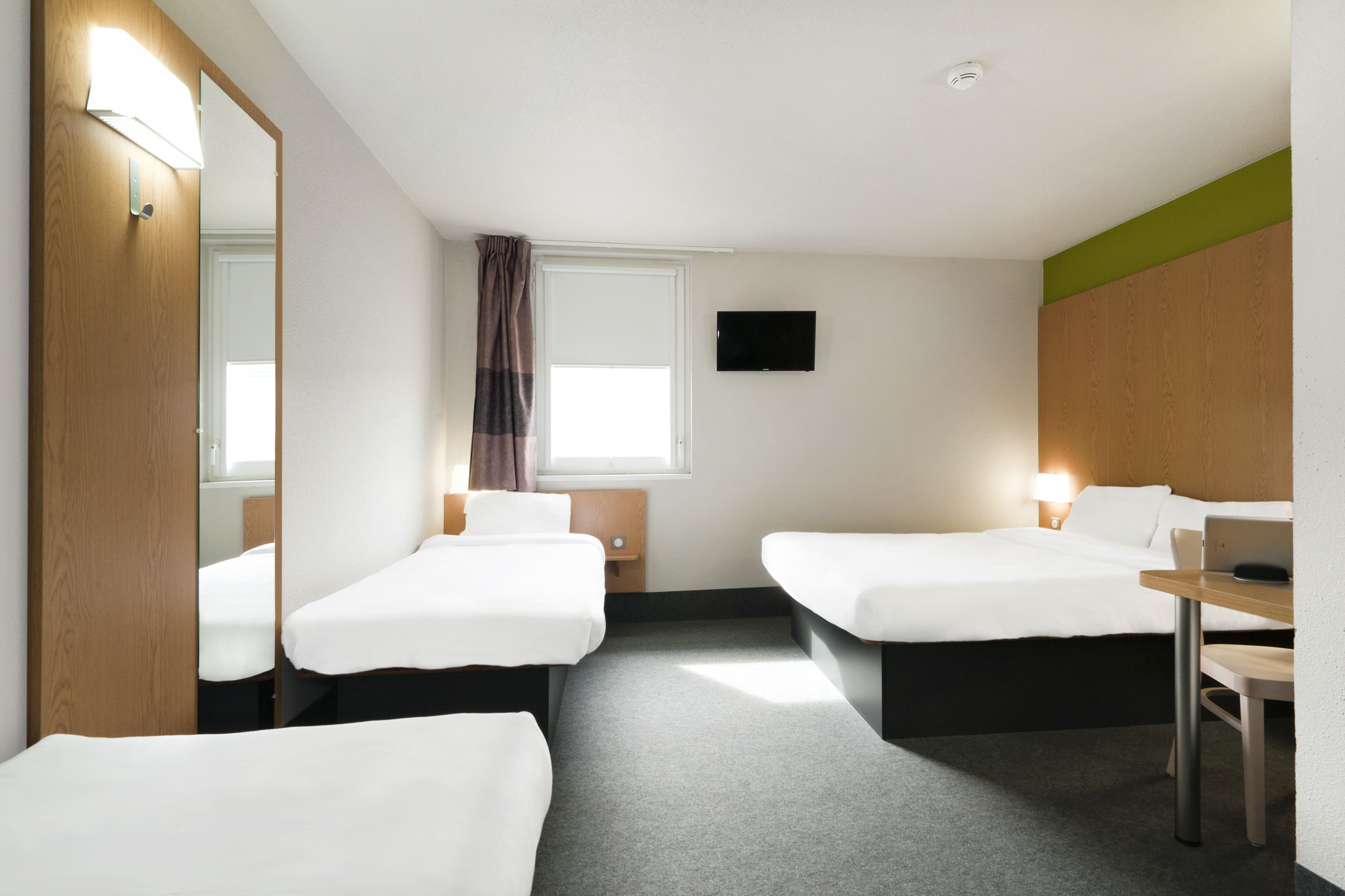 Een hotelkamer met twee enkele bedden, een bureau, een stoel, een televisie en een spiegel.