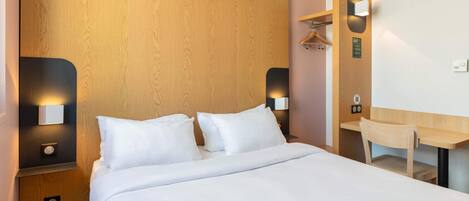 Un hotel moderno con una cama de madera, ropa de cama blanca, mesitas de noche con lámparas, un escritorio de madera y un espejo.