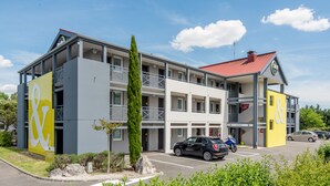 Un hotel de diversos pisos amb una façana prominent de color groc i blanc, balcons i una zona d'aparcament.