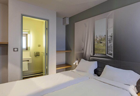 Una habitación de hotel moderna con una cama, una mesita de noche, un espejo y una ventana con vistas a la vegetación.
