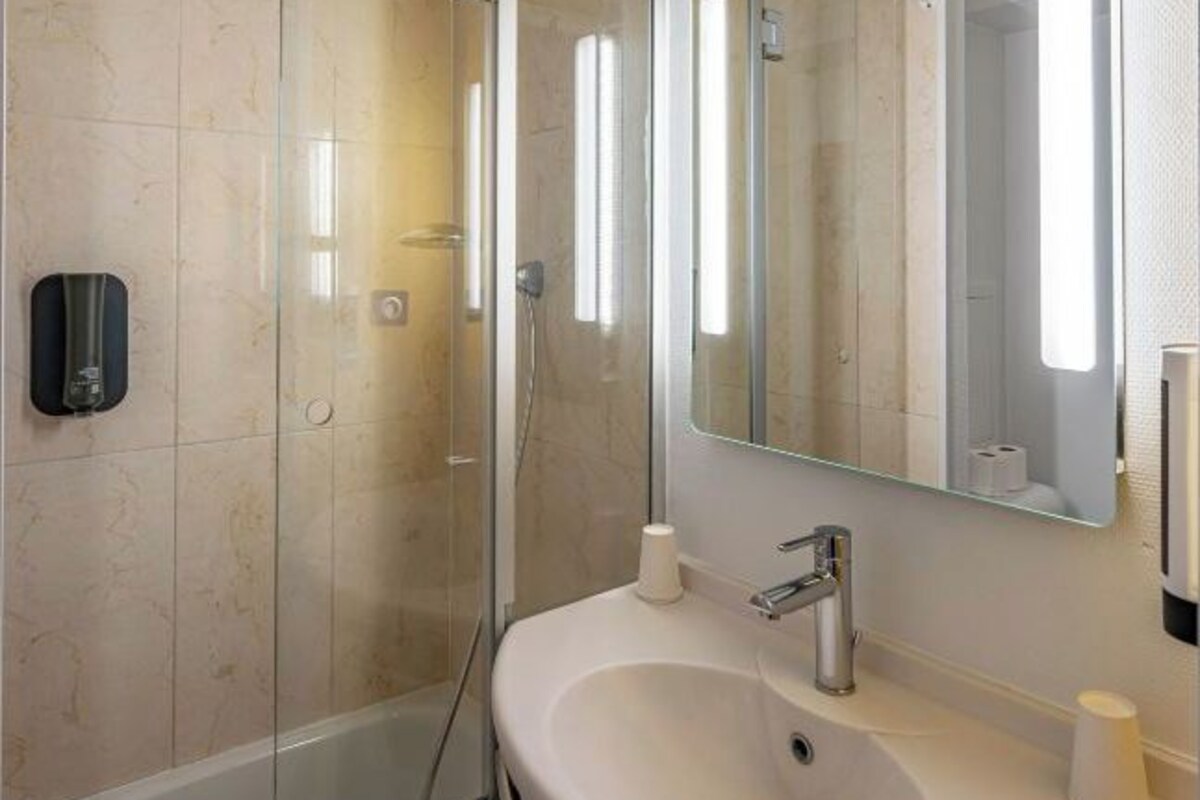 Un baño moderno con ducha de vidrio, lavamanos blanco y un espejo grande.