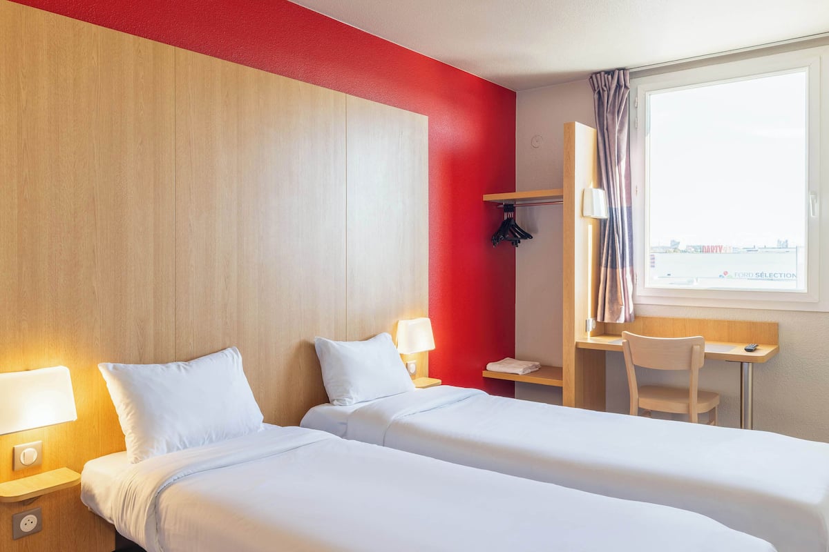 A hotel room with two beds, a desk, a chair, and a window with a view.