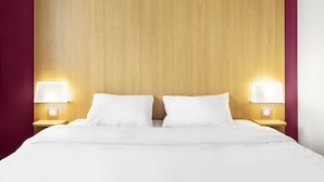 Una habitación de hotel con cabecera de madera, dos lámparas de noche y una cama bien hecha.