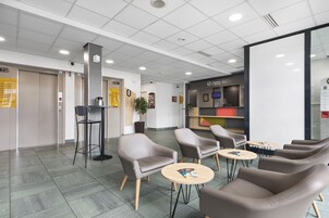 Un área de espera moderna con sillones de cuero, pequeñas mesas redondas y un mostrador de recepción.