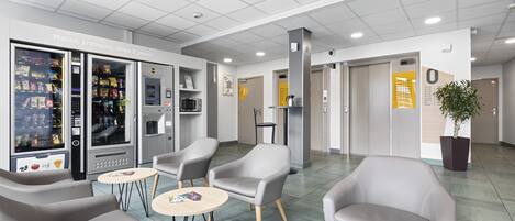A modern lobby with seating areas, vending machines, and a reception desk.