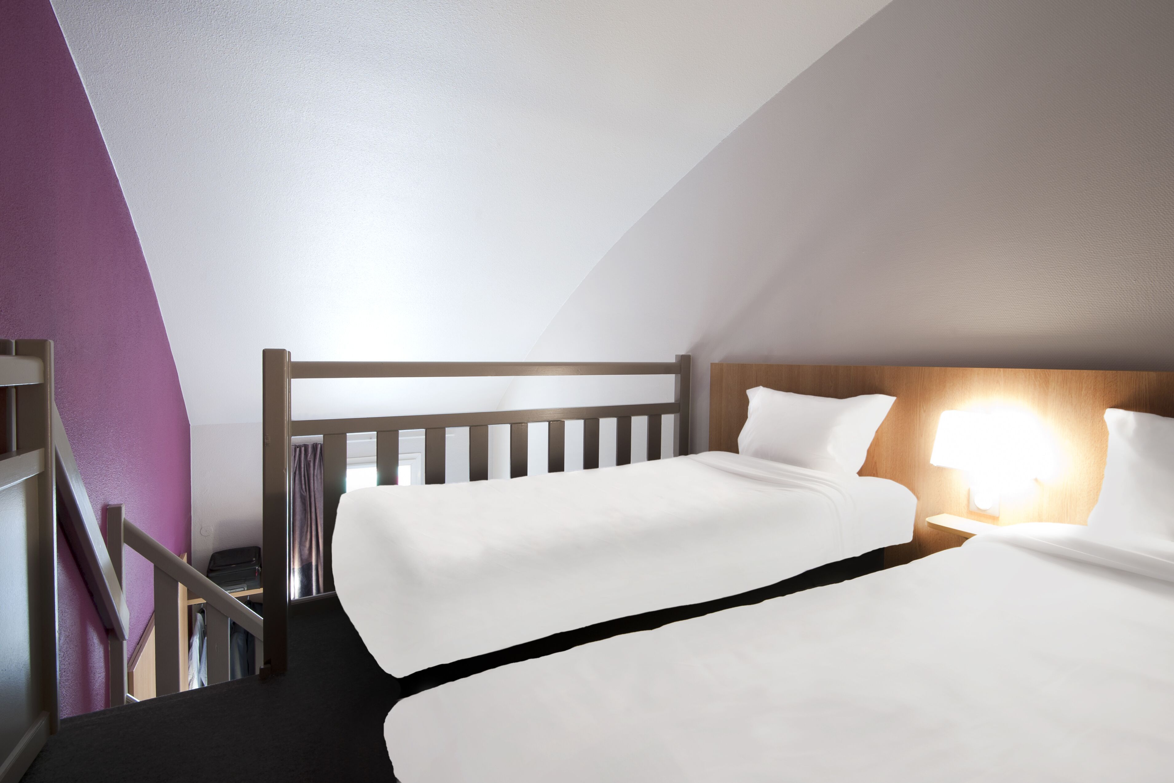 Une chambre d’hôtel avec deux lits, une tête de lit en bois, une table de chevet avec une lampe et un escalier menant à un placard.