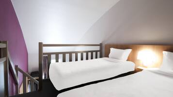 Une chambre d’hôtel avec deux lits, une tête de lit en bois, une table de chevet avec une lampe et un escalier menant à un placard.