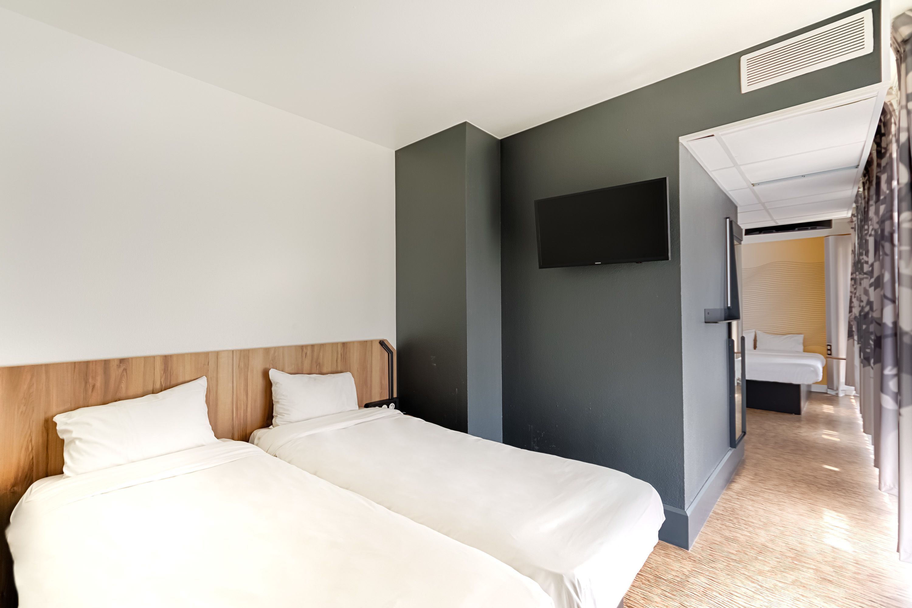 Habitación de hotel moderna con dos camas, un televisor de pantalla plana y un baño visible a través de una puerta abierta.