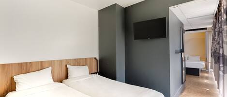 Habitación de hotel moderna con dos camas, un televisor de pantalla plana y un baño visible a través de una puerta abierta.