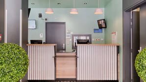 A reception area with a green wall, two reception desks, a digital screen, and a door. - B&B HOTEL Marseille Centre La Joliette (Marseille)