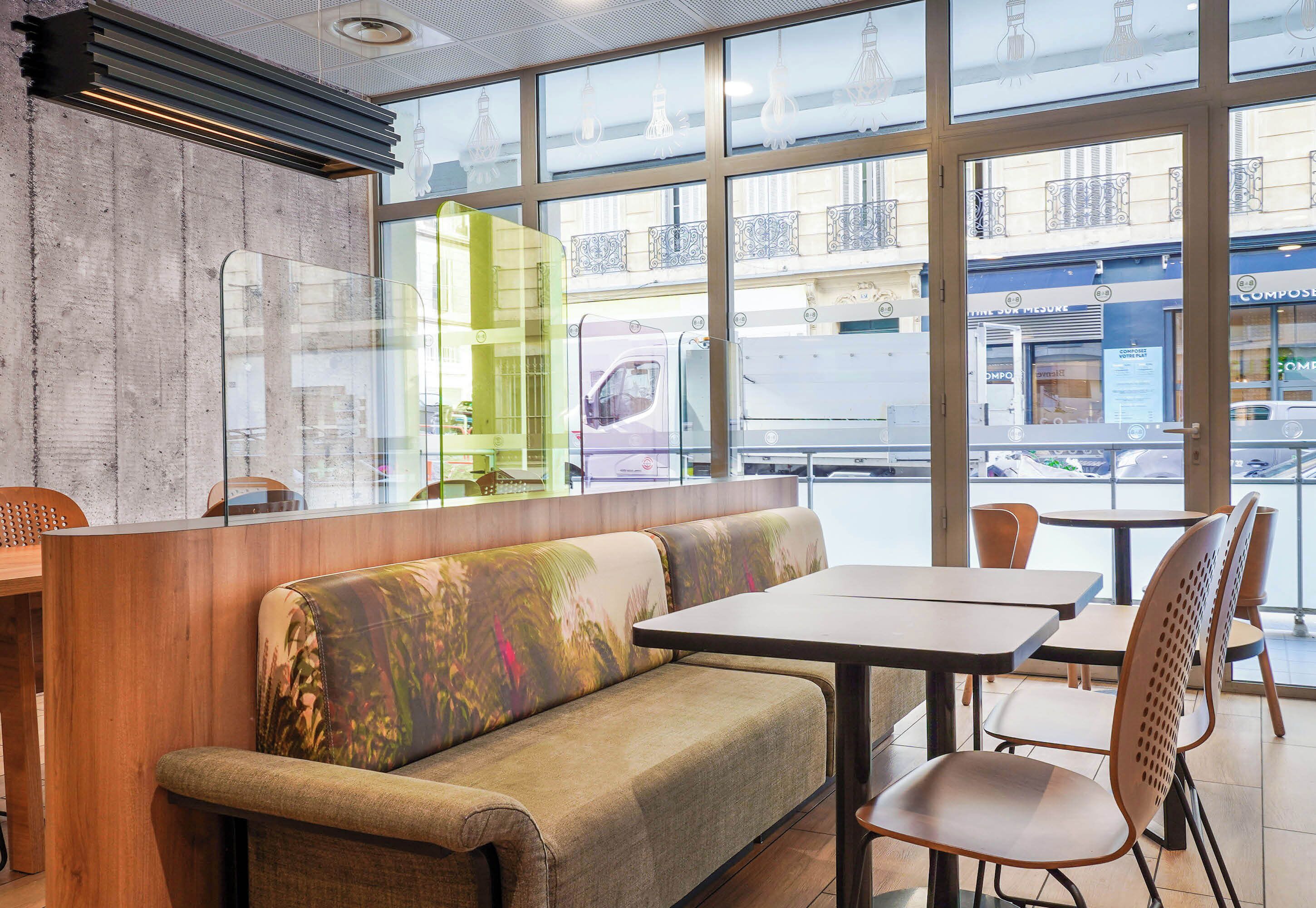 Ein modernes Interieur mit einer Sitzecke, die eine Couch und Tische umfasst, großen Fenstern mit Blick auf die Straße und einer Betonwand mit einer Leuchte.