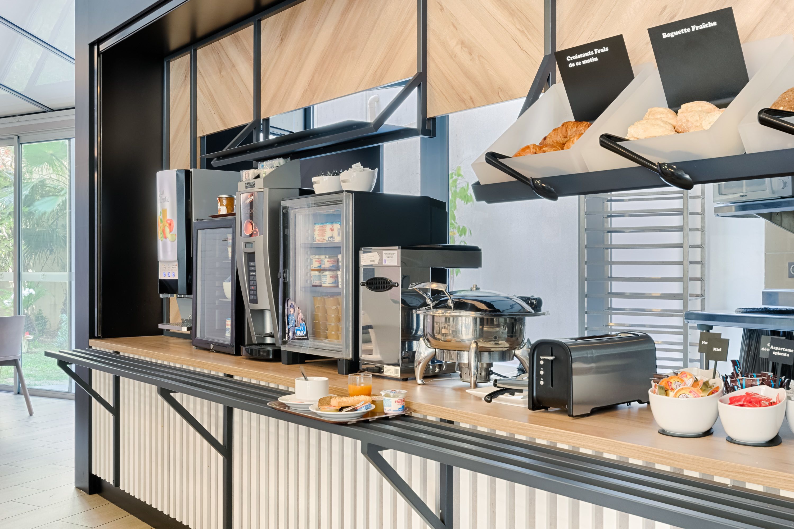 Un bar pour le petit-déjeuner équipé d’une machine à café, d’un grille-pain et de bols remplis de nourriture.