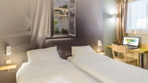 Une chambre d’hôtel avec deux lits, un bureau avec un ordinateur portable, une fenêtre donnant sur un pont et une rivière, et un rideau.