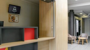 Un espace d’accueil avec un comptoir en bois, un écran numérique affichant le message « Bonjour B&B » et un menu encadré accroché au mur.