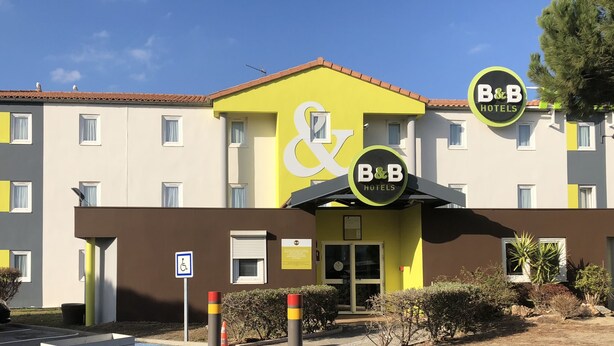 Un hôtel de type « bed and breakfast » avec une façade jaune, de nombreuses fenêtres et un panneau indiquant qu’il est accessible aux personnes à mobilité réduite.