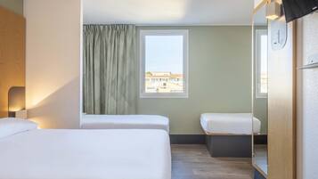 Habitación de hotel con dos camas, una ventana con cortinas, un espejo y un televisor montado en la pared.