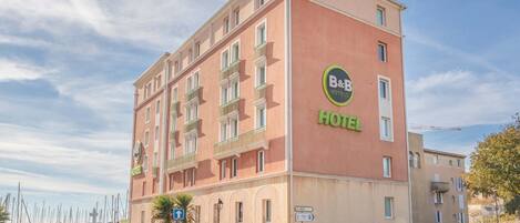 Un hotel B&B con fachada roja, varios balcones y vistas al puerto deportivo.