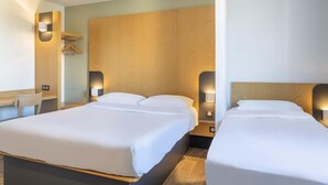 A hotel room with two beds, a wooden headboard, bedside lamps, a wooden desk, and a hanging coat rack. - B&B HOTEL Martigues Port-de-Bouc (Port-de-Bouc)