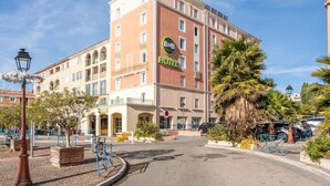 A multi-story hotel with balconies, a central entrance, and a parking area. - B&B HOTEL Martigues Port-de-Bouc (Port-de-Bouc)