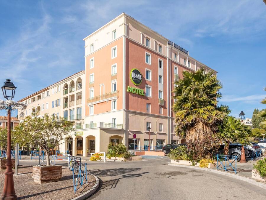 Een hotel met meerdere verdiepingen, balkons, een centrale ingang en een parkeerplaats.