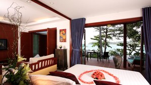 Habitación de hotel con una cama grande, vista al mar, zona de comedor y balcón con mesa y sillas.