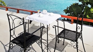 Una terraza con dos sillas de metal negro y una mesa con mantel blanco, con vista a un mar azul claro y una pequeña isla.