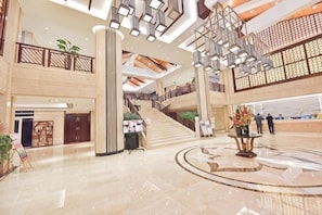 A spacious lobby with a central staircase, a reception desk, and a decorative fountain.